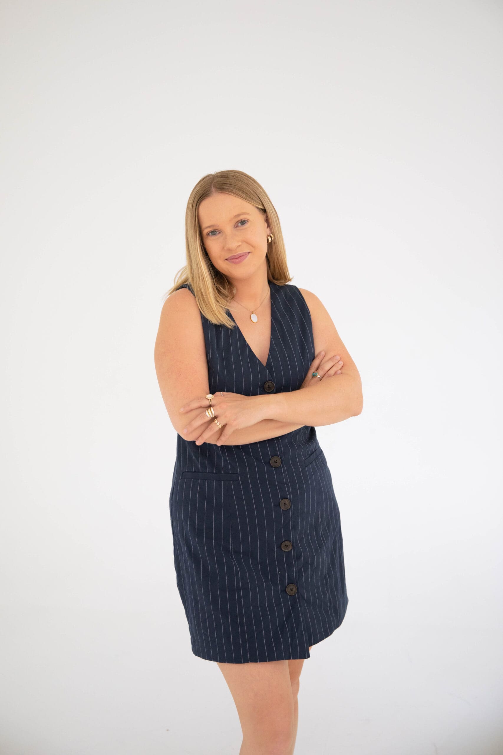 Colorado couples therapist posing confidently in a navy pinstripe dress with arms crossed in a bright neutral studio