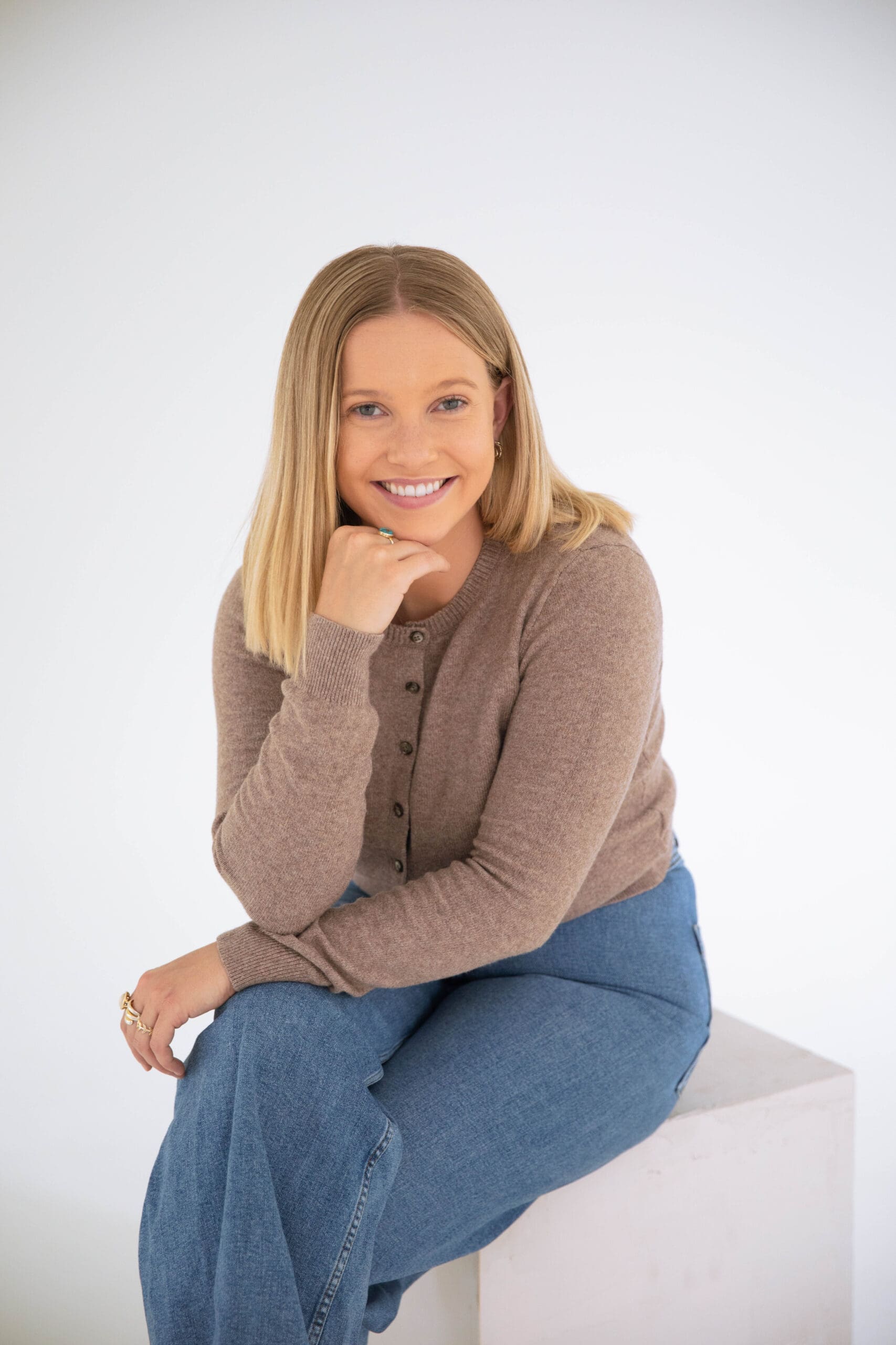 Denver therapist seated on a studio block, smiling toward the camera in a warm and inviting portrait.