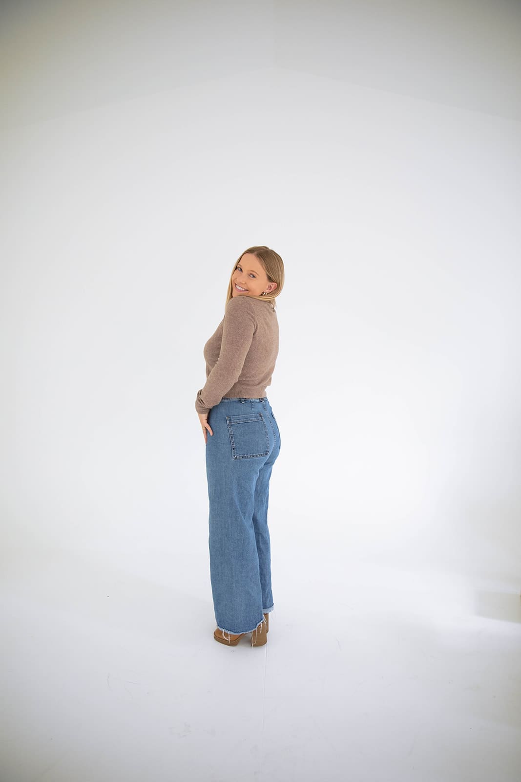 Denver therapist seated standing against a white backdrop, smiling warmly in a relaxed and welcoming portrait.